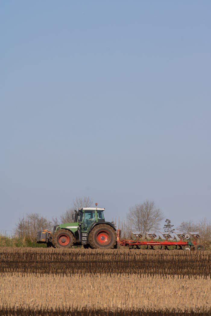 Green tractor plowing a rural field, representing agricultural work and landscape.