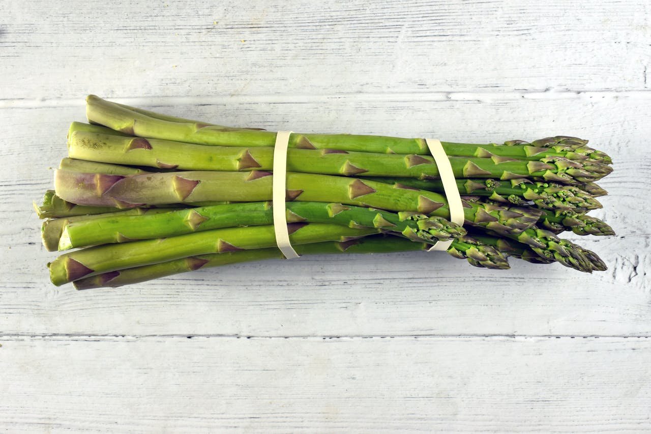 A close-up view of a fresh asparagus bundle on a rustic wooden background, highlighting its vibrant green color.